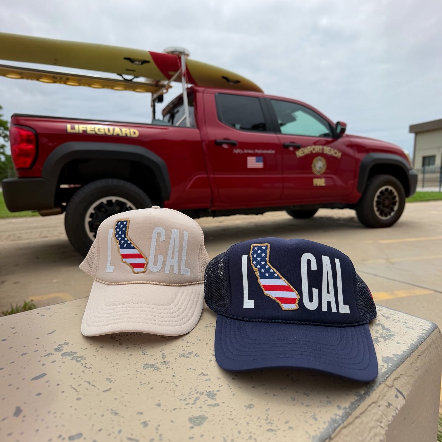 LOCAL CAL trucker hats tan and navy displayed in front of Newport Beach lifeguard truck